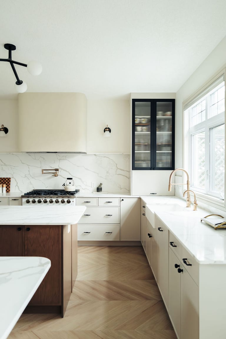 White cabinets and stone counters along a kitchen window with a brass faucet.