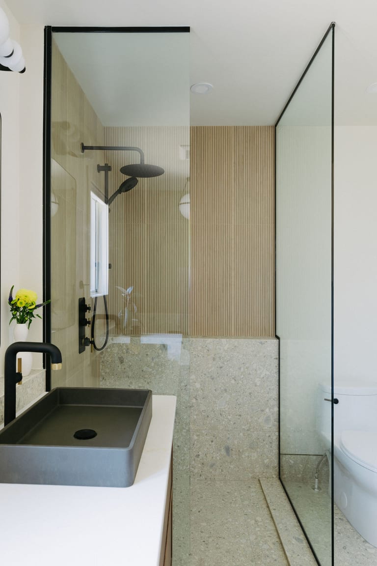A walk in shower with glass panels, fluted wall tile, a stone lower wall and a black rain shower.