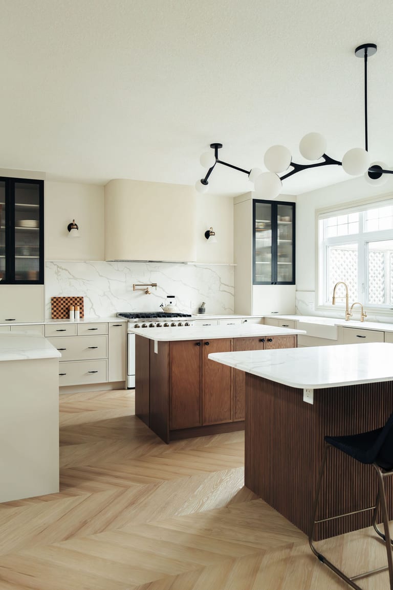 Two kitchen islands in wood, one fluted, on a herringbone floor.