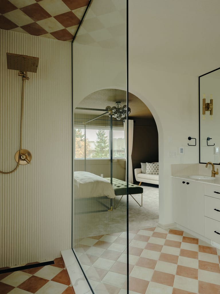 An ensuite with a glass shower, fluted wall tile, a checkered tile floor and ceiling, and a white vanity.