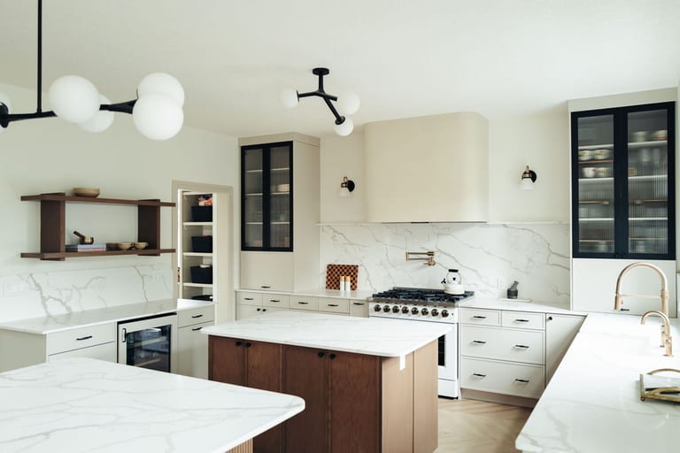White kitchen cabinets with black hardware, glass front upper cabinets and a stone backsplash.