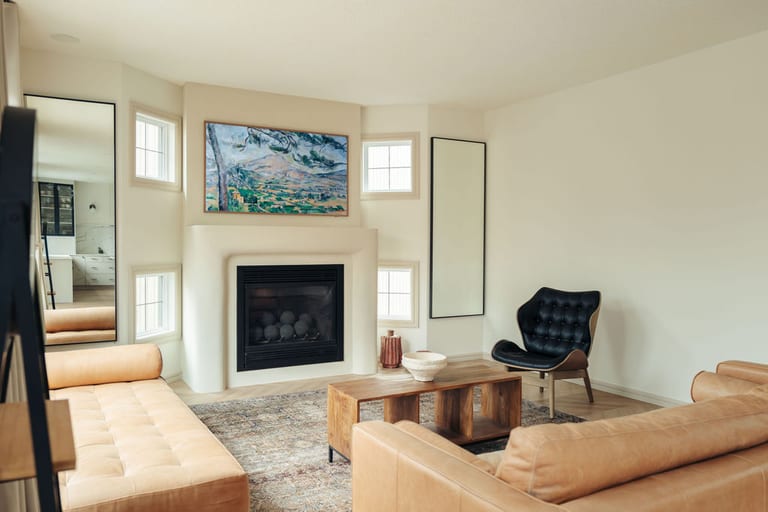 Bright living room with a fireplace, framed art above it, tall windows and a leather sofa.